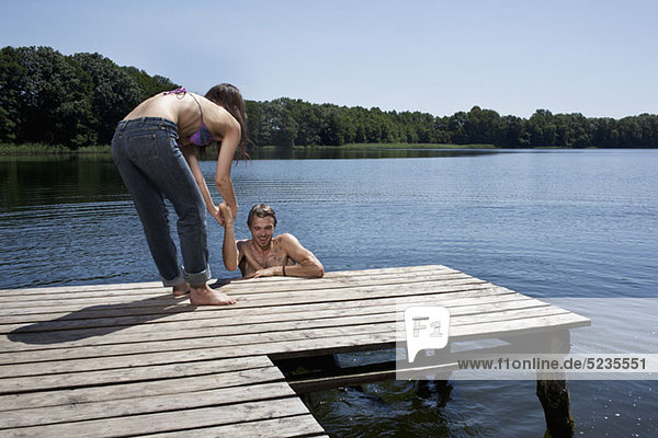 Spaß als Frau hilft dem Mann aus dem Wasser auf dem Steg
