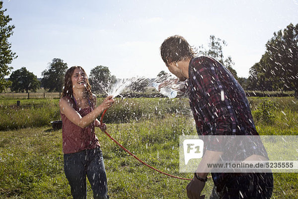 Girl sprays guy with hose on field