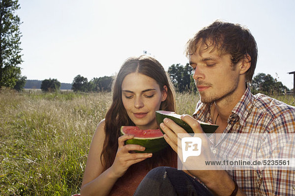 Couple in field eating a melon