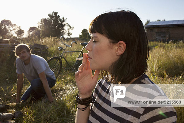 Mädchen rauchen im Feld als Mann im Hintergrund Uhren
