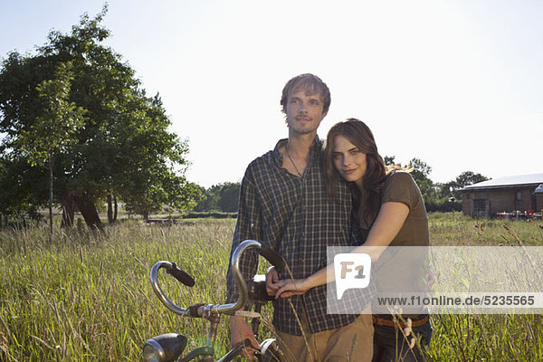 Couple with arms around each other walk through field with bike
