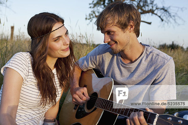 Man plays guitar to his girlfriend in field