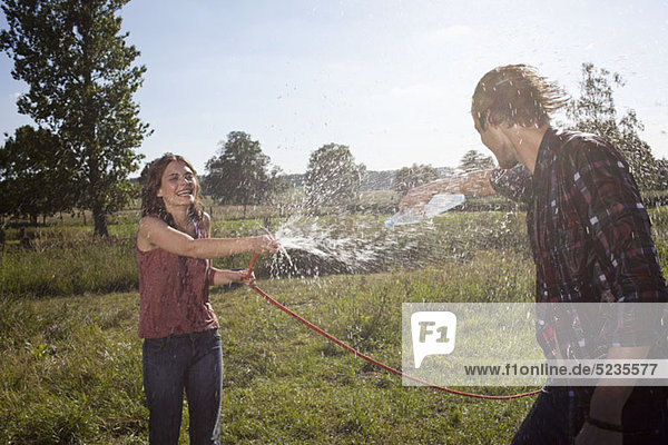 Girl sprays guy with hose in a field