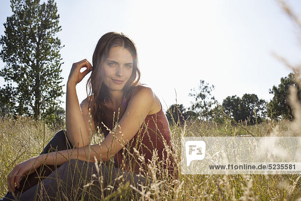 Girl sitting amongst timothy grass in the sunshine playing with her hair