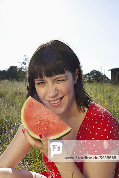 Girl sitting in field with a slice of melon in her hand