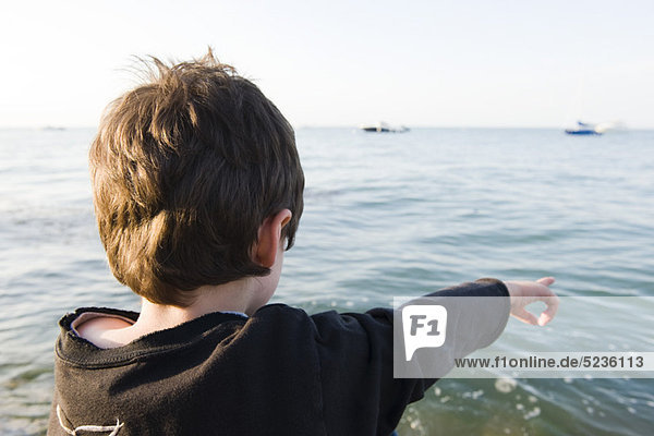 Junge blickt auf den Ozean  zeigt auf das Meer