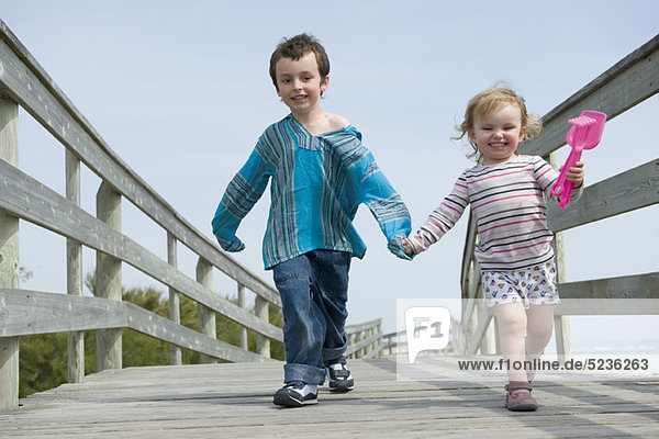 Junge Geschwister  die Hand in Hand auf der Strandpromenade gehen