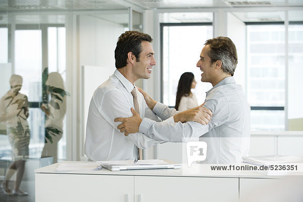Businessmen holding each other's arms with excitement