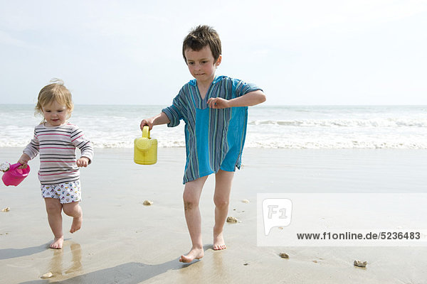 Junge Geschwister  die auf nassem Sand am Strand spazieren gehen