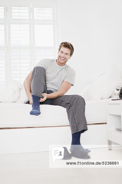 Mann zieht Socken im Bett an