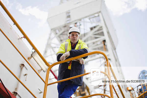 Worker leaning on railing of oil rig