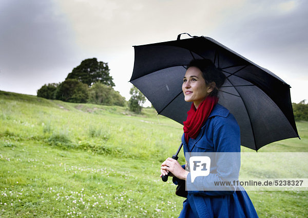 Frau hält Regenschirm im Feld