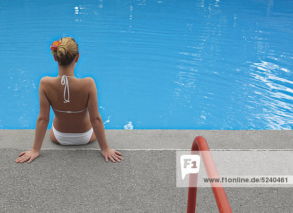 Frau sitzt in Bikini an Pool
