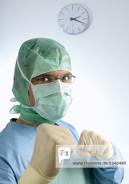 Chirurg mit Haube und Mundschutz  geballte Fäuste  Porträt