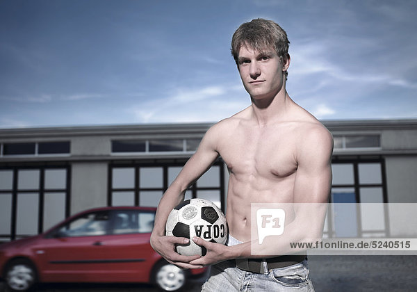 Junger Mann mit Fußball auf Garagenplatz  Halbporträt