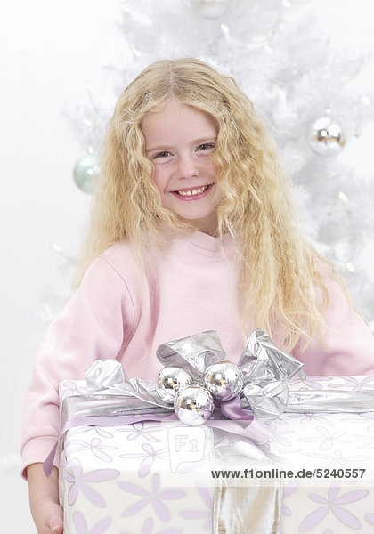 Kleines Mädchen mit großem Paket vor Weihnachtsbaum  lacht