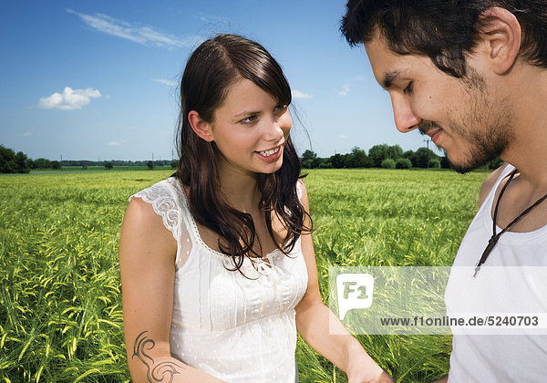 Junges Paar steht in Getreidefeld  er ist verlegen