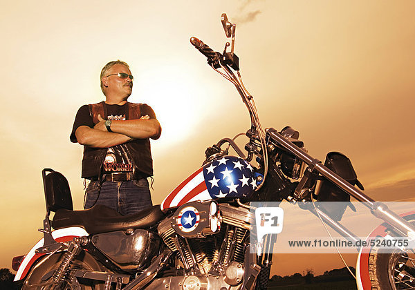 Älterer Motorradfahrer steht neben Motorrad in US-Bemalung