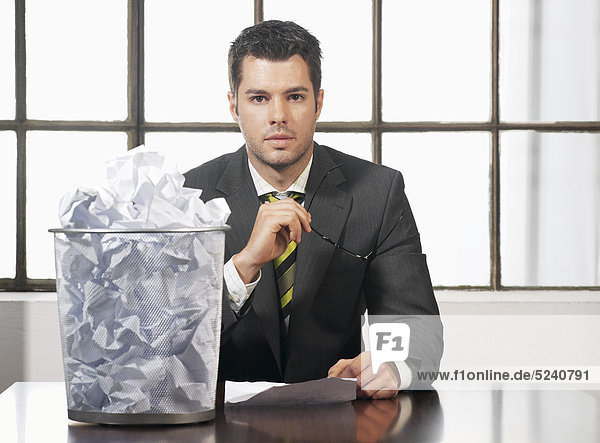 Mann sitzt mit vollem Papierkorb an Schreibtisch