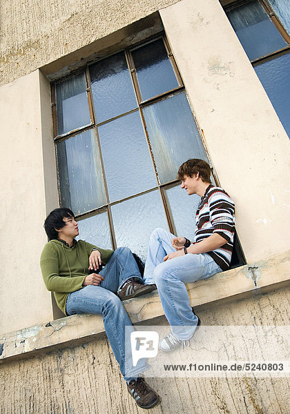 Zwei junge Männer  einer asiatisch  sitzen aussen auf Fenstersims