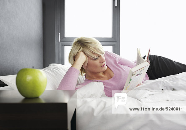 Frau liegt in Bett  liest Buch