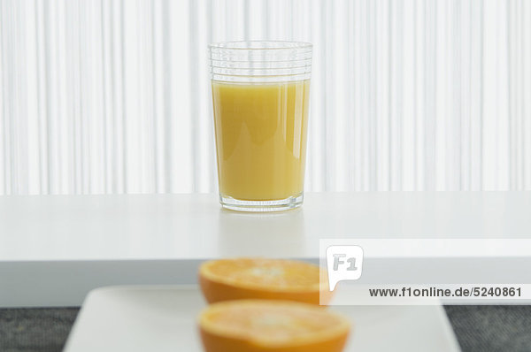 Ein Glas Orangensaft mit einer halben Orange davor.