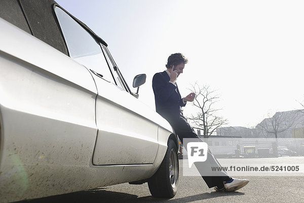 Mittlerer Erwachsener Mann  der sich auf Oldtimer stützt und mit dem Handy spricht