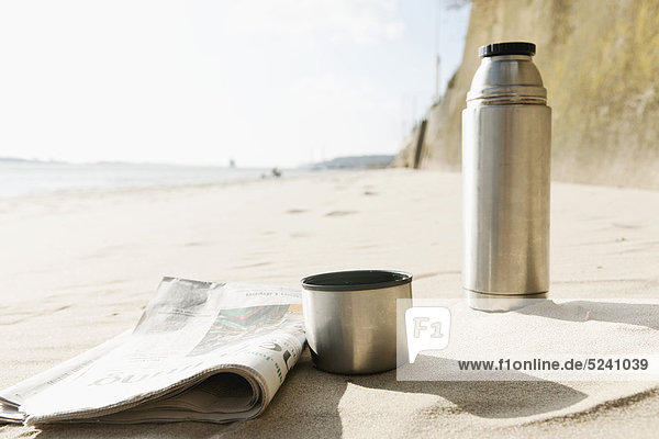 Deutschland  Hamburg  Nahaufnahme von Zeitung und Thermoskanne am Strand an der Elbe