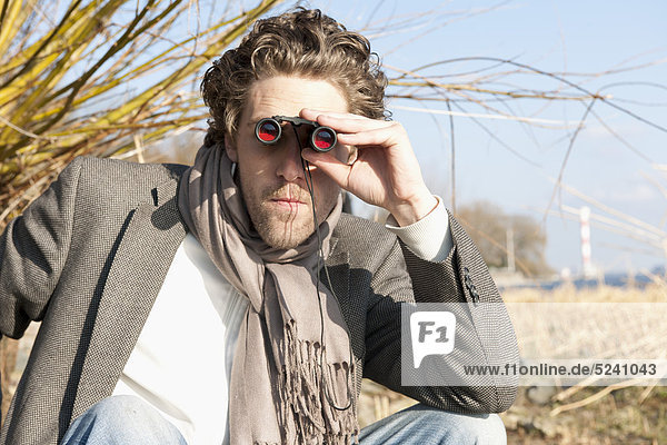 Mann schaut durchs Fernglas an der Elbe