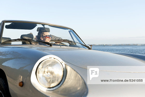 Mann im klassischen Cabriolet an der Elbe sitzend