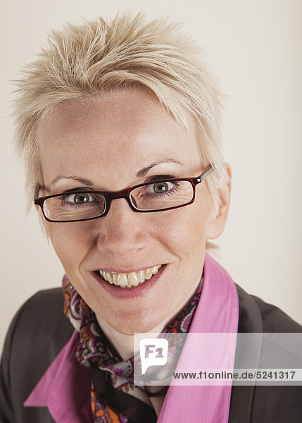Nahaufnahme einer reifen Frau im Business-Anzug vor weißem Hintergrund lächelnd Portrait