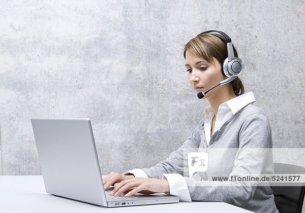 Frau sitzt in Büro mit Headset an Laptop