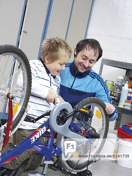 Vater und Sohn reparieren Fahrrad Junge schraubt Rad fest