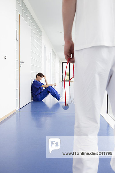 Germany  Bavaria  Diessen am Ammersee  Young female doctor sitting in corridor and male doctor standing in foreground