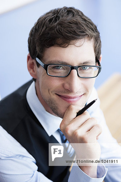 Deutschland  Bayern  Diessen am Ammersee  Nahaufnahme eines Geschäftsmannes in dicker Brille mit Kugelschreiber  lächelnd  Porträt