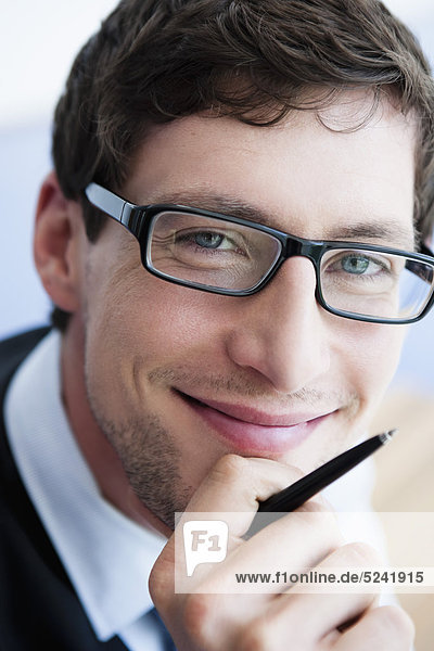 Germany  Bavaria  Diessen am Ammersee  Close up of businessman in thick spectacles holding pen  smiling  portrait