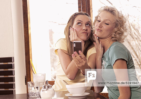 Zwei junge Frauen in Cafe  fotografieren sich mit Handy