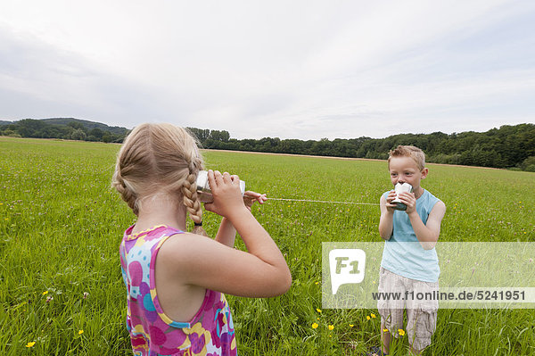 Deutschland  Nordrhein-Westfalen  Hennef  Junge und Mädchen auf der Wiese spielen mit Blechdose telefonieren