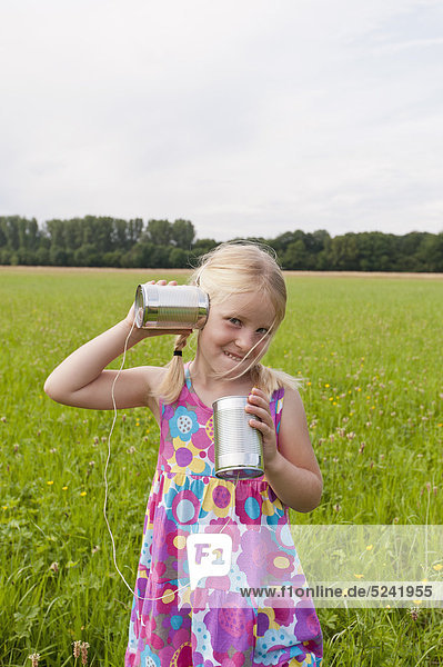 Germany  North Rhine-Westphalia  Hennef  Girl standing in meadow and playing with tin can phone