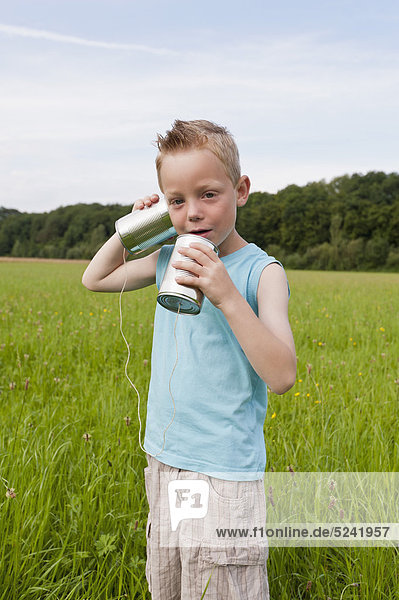 Germany  North Rhine-Westphalia  Hennef  Boy standing in meadow and playing with tin can phone