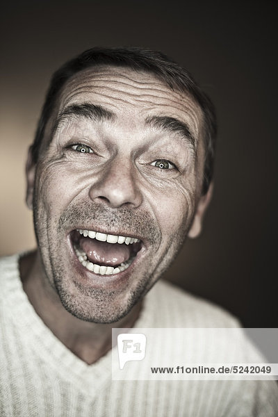 Close up of mature man making funny faces against black background  laughing  portrait