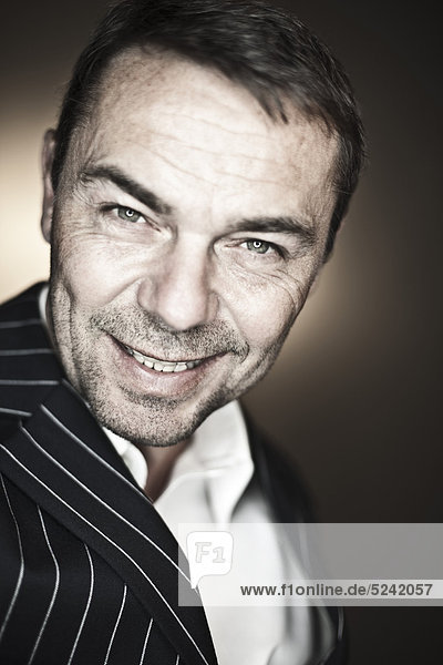 Close up of mature man in suit against black background  smiling  portrait