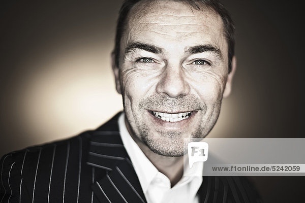 Close up of mature man in suit against black background  smiling  portrait
