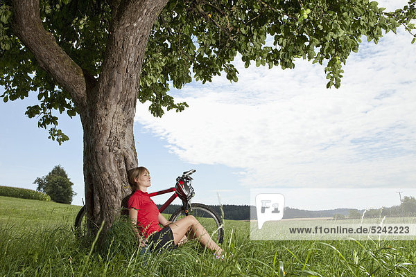 Young woman sitting against tree with mountain bike