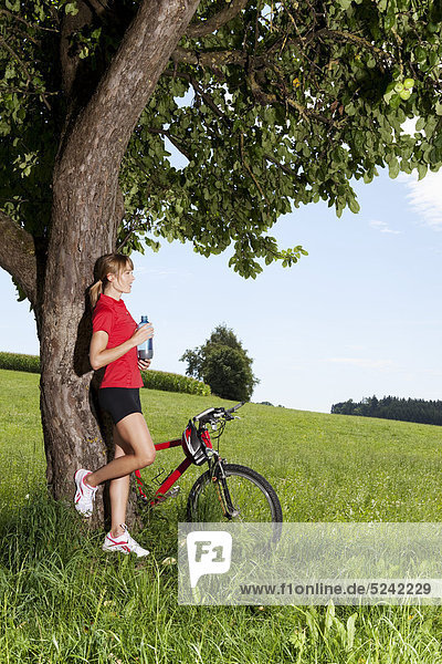 Junge Frau an Baum gelehnt mit Mountainbike