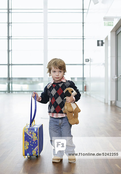 Kleiner Junge mit einem Stofftier zieht seinen Kinderkoffer  Flughafen