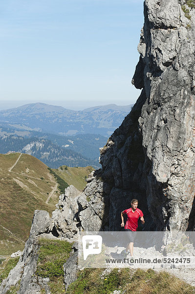 Österreich  Kleinwalsertal  Junge Frau beim Laufen auf dem Bergweg in der Nähe von Felsen