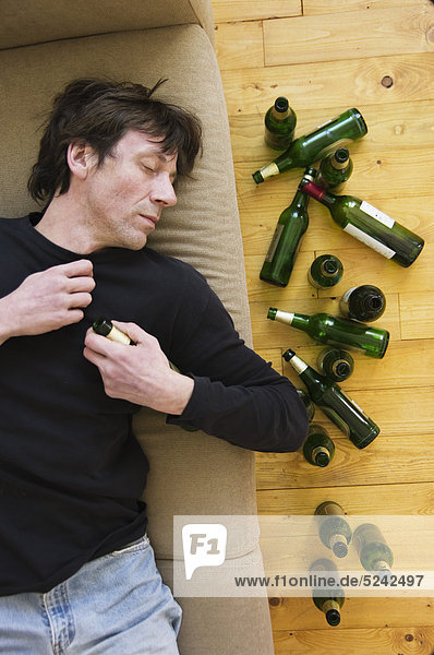 Drunk man lying on sofa with empty beer bottles