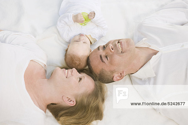 Deutschland  Bayern  Vater  Mutter und Tochter auf Decke liegend  lächelnd