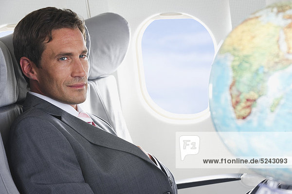 Deutschland  Bayern  München  Mittlerer Erwachsener Geschäftsmann mit Blick auf den Globus in der Business Class Flugzeugkabine